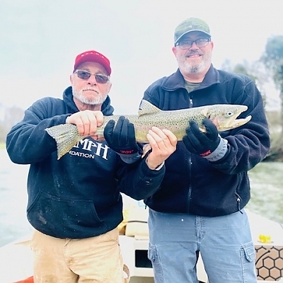 Two gentlemen hold up fish caught on fishing trip.